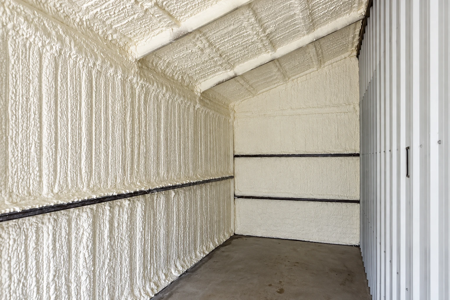 Small interior space with thick white spray foam covering the walls and ceiling beside a corrugated metal wall.
